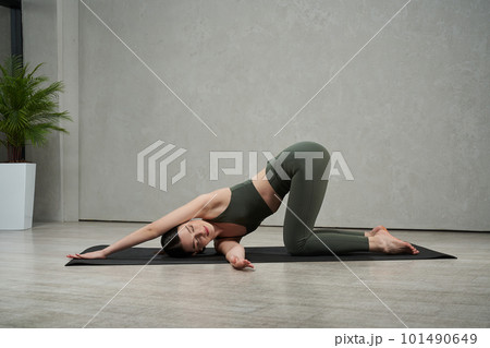 Side view of slim, flexible female athlete working out, exercising, training indoors. Young, brunette girl stretching barefoot. Concept of athletics, sport and wellbeing. 101490649