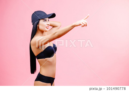 Young woman in bikini in summer holidays standing and pointing finger to the side on pink background in studio Young woman in bikini in summer holidays standing and pointing finger to the side on pink background in studio 101490778