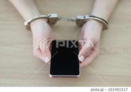 Woman in handcuffs holds modern smartphone sitting at table Woman in handcuffs holds modern smartphone sitting at table 101491517