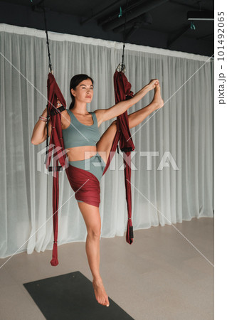 A girl does yoga in a hanging hammock in the gym. Fly yoga in the gym A girl does yoga in a hanging hammock in the gym. Fly yoga in the gym 101492065