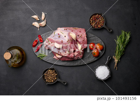 A piece of pork ham on a black board and spices olive oil, salt, rosemary branch and pepper 101493156