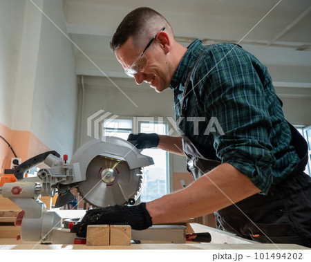 Master cuts the board with a circular saw in the workshop. Master cuts the board with a circular saw in the workshop. 101494202