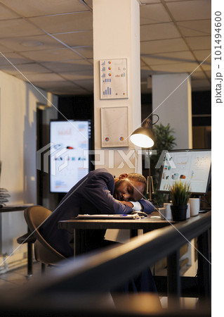 Hardworking entrepreneur falling asleep on table in startup office after finishing financial report. Workaholic executive manager working overtime at workspace, planning company investment strategy 101494600