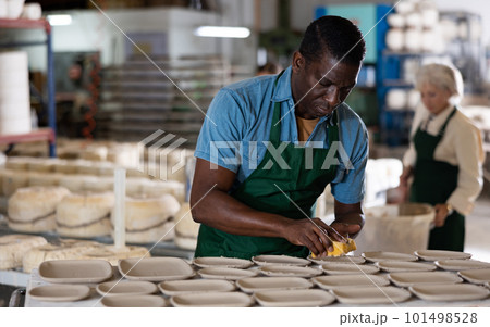 African american man using foam sponge smooths out roughness and irregularities on freshly made pottery 101498528