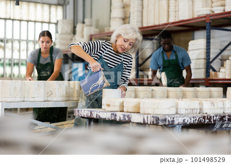 Mature worker pours slip mass from jug into plaster mold in pottery factory 101498529