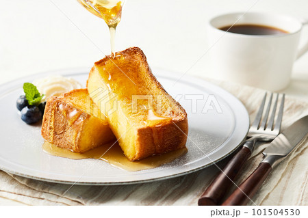 フレンチトーストに蜂蜜を垂らす。お皿の上にブルーベリー、生クリーム フレンチトーストに蜂蜜を垂らす。お皿の上にブルーベリー、生クリーム 101504530