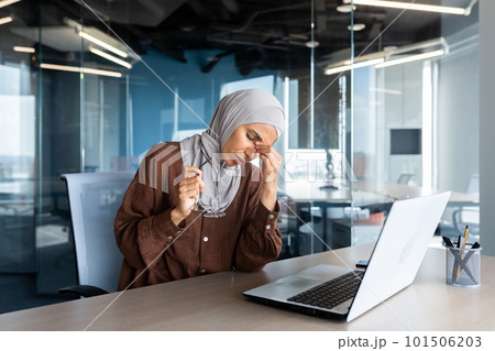Tired and overworked business woman in hijab at workplace, muslim woman massaging eyes with glasses off, female worker working late on project. 101506203
