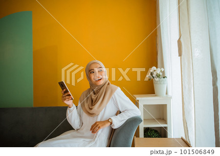 Asian veiled woman casually sitting on sofa using cell phone 101506849