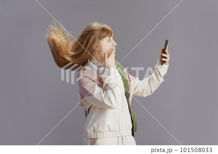 surprised girl in beige tracksuit using phone 101508033