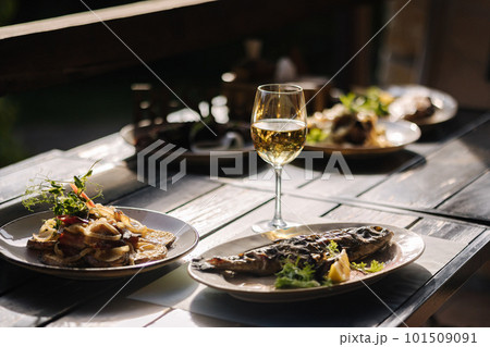 Dinner on summer terrace. Several dishes of fish and some meat in restaurant. Glasses with vine 101509091
