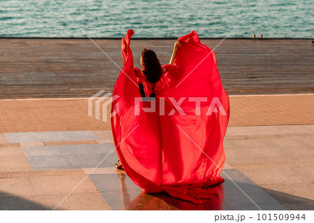 Sunrise red dress. A woman in a long red dress against the backdrop of sunrise, bright golden light of the sun's rays. The concept of femininity, harmony. 101509944