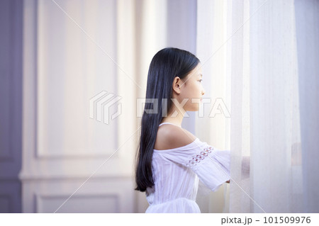 beautiful little asian girl with long black hair looking out of window in bedroom beautiful little asian girl with long black hair looking out of window in bedroom 101509976