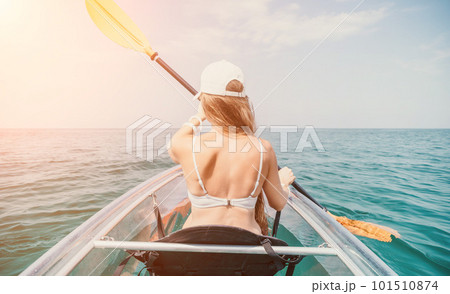 Woman in kayak back view. Happy young woman with long hair floating in transparent kayak on the crystal clear sea. Summer holiday vacation and cheerful female people relaxing having fun on the boat 101510874