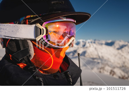 Profile of a female skier in ski goggles in the mountains. A woman in a sports ski jacket and snowboard sunglasses looks away. Sportswear and fashion for winter sports, ski resort 101511726