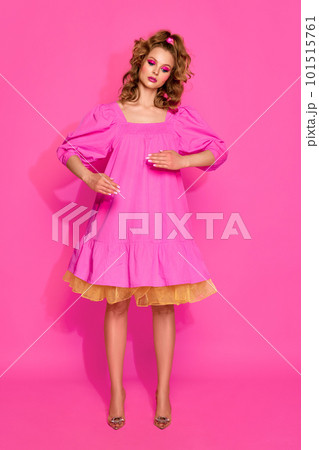 One beautiful blond woman, girl with bright makeup wearing doll dress posing with emotionless face over pink studio background. Living doll 101515761