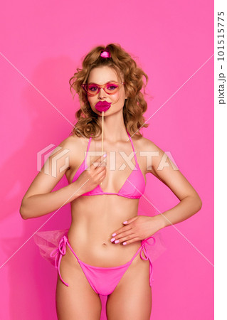 Portrait of young adorable girl wearing swimsuit and posing with candy instead of lips over pink studio background. Funny face Portrait of young adorable girl wearing swimsuit and posing with candy instead of lips over pink studio background. Funny face 101515775