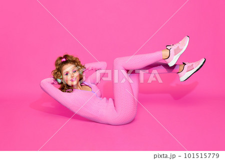 One young sporty girl wearing pink sport suit and headphones training over pink studio background. Abs workout 101515779