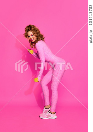 One young, gorgeous sporty girl wearing pink sport suit training with dumbbells over pink studio background. Female workout One young, gorgeous sporty girl wearing pink sport suit training with dumbbells over pink studio background. Female workout 101515782
