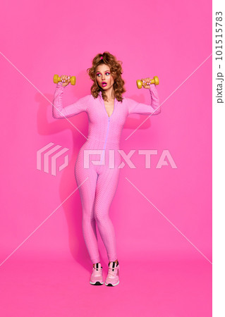 One young, gorgeous sporty girl wearing pink sport suit training with dumbbells over pink studio background. Female workout 101515783