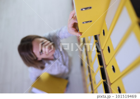 Woman reaches hand to get yellow folder on upper shelf 101519469