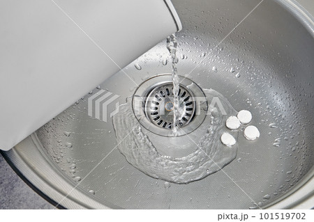 Hot water is poured from a white electric kettle into a metal kitchen sink filled with disinfectant tablets Hot water is poured from a white electric kettle into a metal kitchen sink filled with disinfectant tablets 101519702