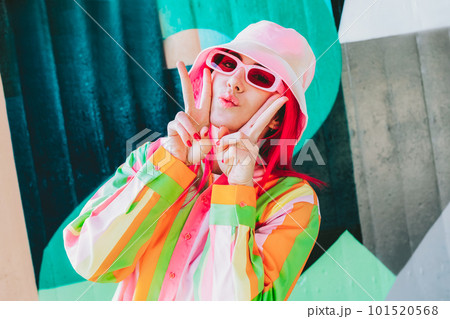 Urban Fresh street fashion look. Vanilla Girl. Kawaii vibes. Candy colors design. Bucket hat trends. Young woman with pink hair and sun glasses in multicolor strippled shirt on the wall background Urban Fresh street fashion look. Vanilla Girl. Kawaii vibes. Candy colors design. Bucket hat trends. Young woman with pink hair and sun glasses in multicolor strippled shirt on the wall background 101520568