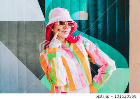 Urban Fresh street fashion look. Vanilla Girl. Kawaii vibes. Candy colors design. Bucket hat trends. Young woman with pink hair and sun glasses in multicolor strippled shirt on the wall background Urban Fresh street fashion look. Vanilla Girl. Kawaii vibes. Candy colors design. Bucket hat trends. Young woman with pink hair and sun glasses in multicolor strippled shirt on the wall background 101520569