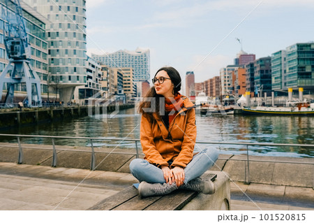 Smiling young woman sitting on sthe bench at Hafencity, Hamburg, Germany 101520815