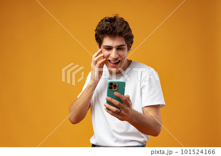 Young happy man looking at his phone against yellow background 101524166