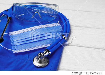 Doctor medical uniform with stethoscope and face mask on white wooden background Doctor medical uniform with stethoscope and face mask on white wooden background 101525222
