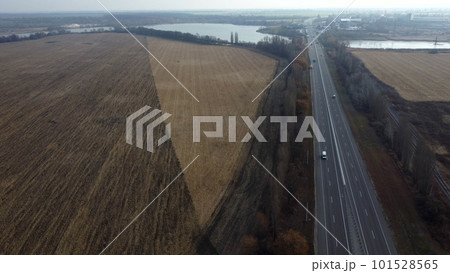 Large plowed field with plowed land and yellow dry straw after harvesting wheat, a lake, a highway with driving cars on an autumn day. Agro industrial agricultural farm landscape. Aerial drone view. Large plowed field with plowed land and yellow dry straw after harvesting wheat, a lake, a highway with driving cars on an autumn day. Agro industrial agricultural farm landscape. Aerial drone view. 101528565