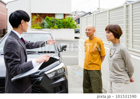 屋外で自動車販売員から説明を聞く老夫婦 101531590