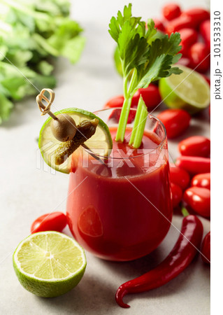 Bloody Mary cocktail garnished with gherkin, olive, lime, and celery on a white stone table. 101533310