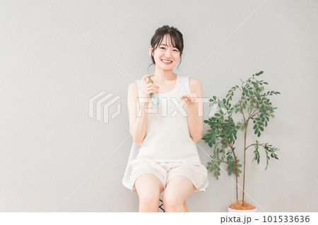 化粧水・美白美容液・日焼け止めを使う椅子に座った笑顔のアジア人女性 化粧水・美白美容液・日焼け止めを使う椅子に座った笑顔のアジア人女性 101533636