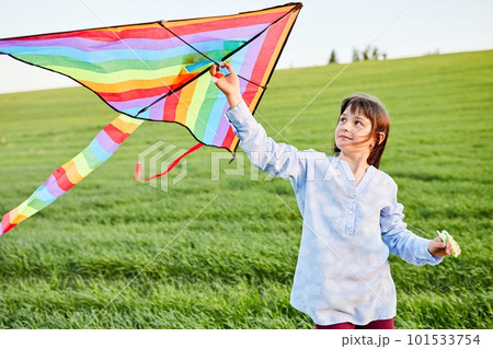 Little happy girl running with kate in hands on green wheat field. Large colored rainbow kite with long tail. 101533754