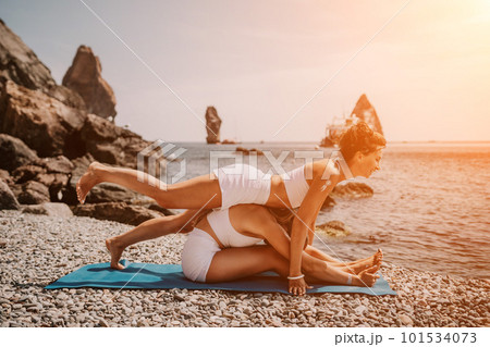 Woman sea yoga. Two Happy women meditating in yoga pose on the beach, ocean and rock mountains. Motivation and inspirational fit and exercising. Healthy lifestyle outdoors in nature, fitness concept. 101534073