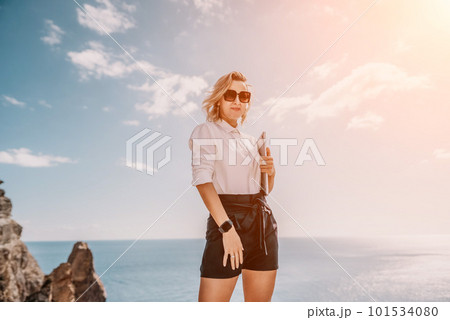 Digital nomad, Business woman working on laptop by the sea. Pretty lady typing on computer by the sea at sunset, makes a business transaction online from a distance. Freelance, remote work on vacation 101534080