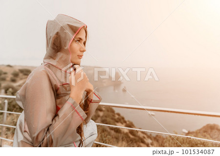 Woman rain umbrella. Happy woman portrait wearing a raincoat with transparent umbrella outdoors on rainy day in park near sea. Girl on the nature on rainy overcast day. Woman rain umbrella. Happy woman portrait wearing a raincoat with transparent umbrella outdoors on rainy day in park near sea. Girl on the nature on rainy overcast day. 101534087