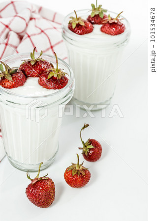 Dessert yogurt and strawberry layers in a glass on a red striped napkin on a white background Dessert yogurt and strawberry layers in a glass on a red striped napkin on a white background 101534678
