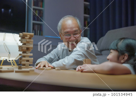 Happy grandparents Asian family enjoy playing toy block with little daughter and mother together at home night time, Smiling parent having fun play build constructor tower of wooden blocks, education 101534945