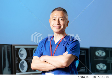 腕組みをしながら視線を向けるスクラブ着用のシニア男性 101536250