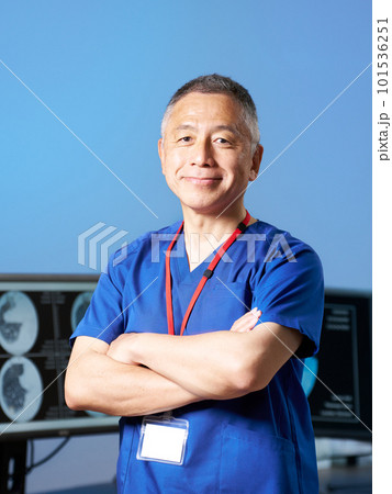 腕組みをしながら視線を向けるスクラブ着用のシニア男性 101536251