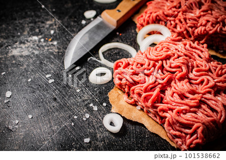 Fresh minced meat on paper on a table with a knife and onion rings. 101538662