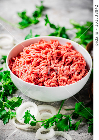 Minced meat in a bowl on a table with parsley and onion rings. Minced meat in a bowl on a table with parsley and onion rings. 101538842