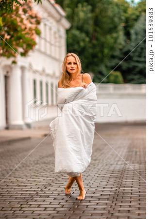Woman city blanket. Morning in the big city. A blonde woman in a white blanket is enjoying in the city center. Photographed for social media Woman city blanket. Morning in the big city. A blonde woman in a white blanket is enjoying in the city center. Photographed for social media 101539383