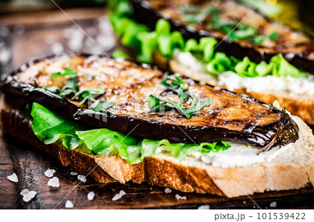 A fragrant sandwich with grilled eggplant on a cutting board. 101539422