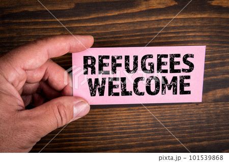 Refugees Welcome. Text on pink paper. Wood texture background Refugees Welcome. Text on pink paper. Wood texture background 101539868