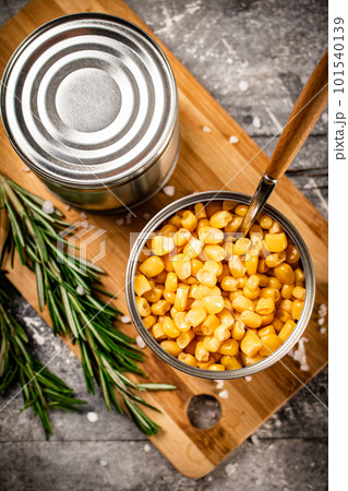 A tin can of canned corn on a cutting board. 101540139