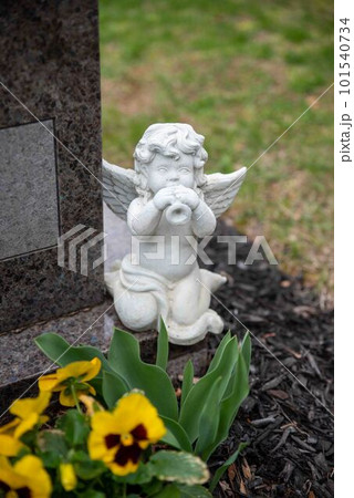 A small white angel statue plays a horn on a cemetery gravestone 101540734