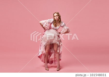 Portrait of charming blond lady, queen wearing dress and standing with upset face on pink studio background. Naughty princess 101548031